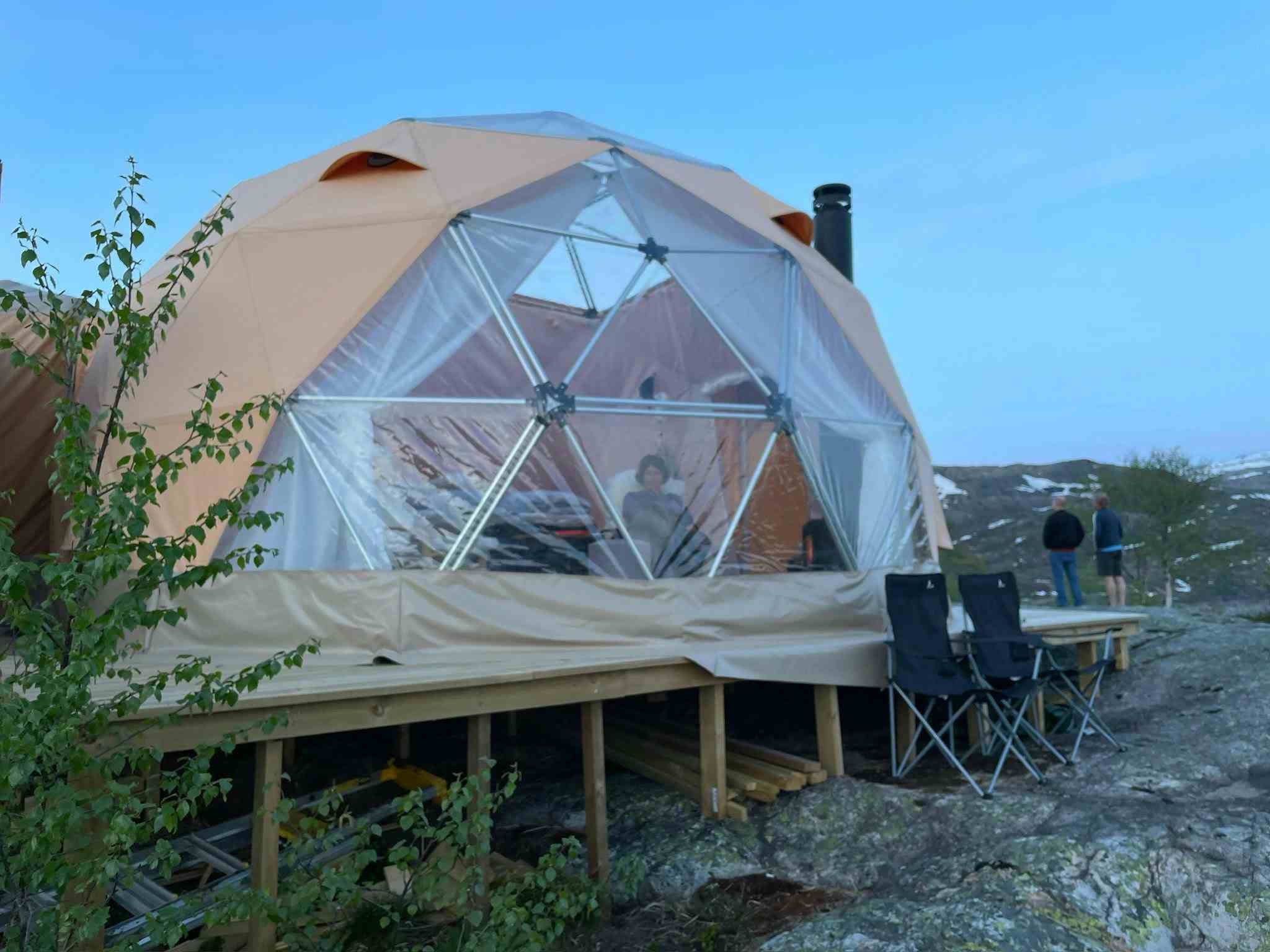 To personer som sitter inne i glamping-teltet og nyter utsikten over Saudafjellet.