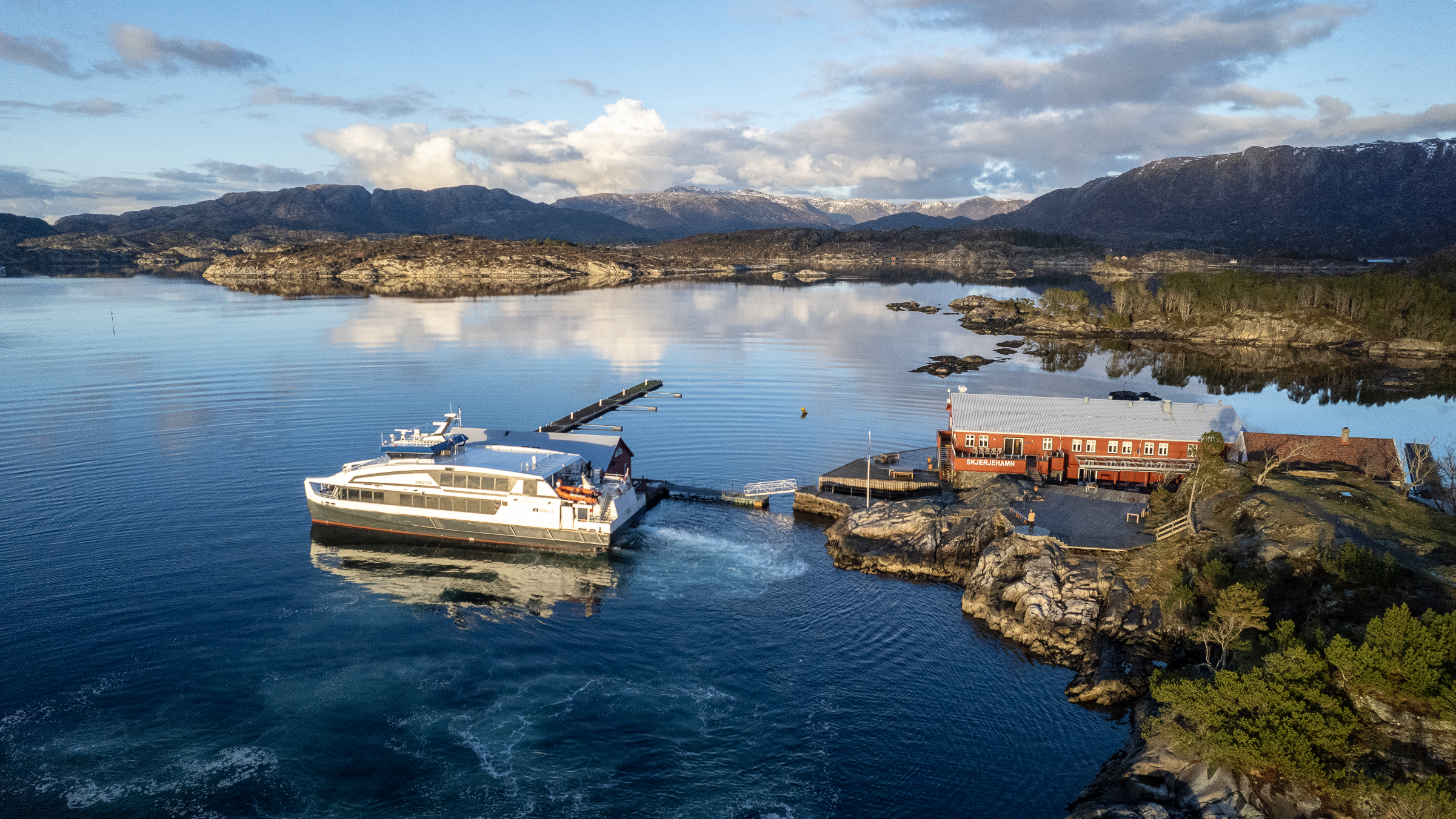 ein stor båt ligg ved kai på Skjerjehamn. det er blått hav rundt, og eit hotell som ligg heilt ved sjøkanten